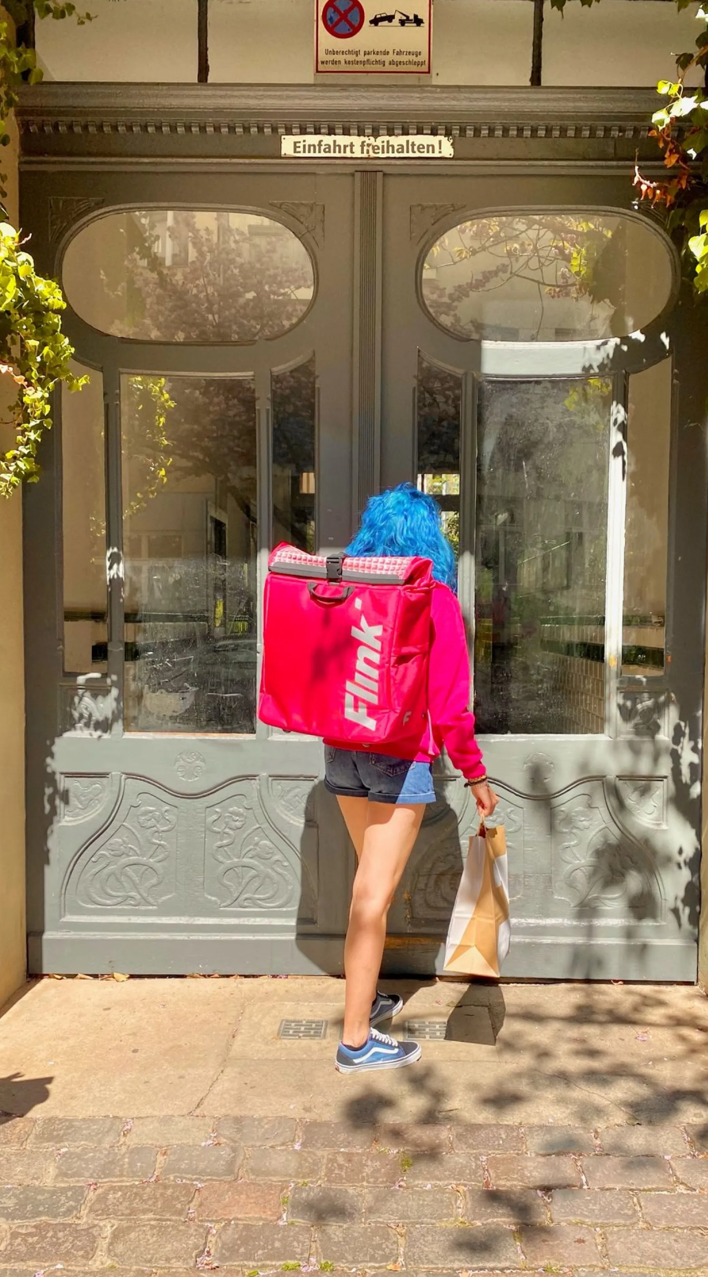 Flink courier carrying a delivery bag outside a storefront